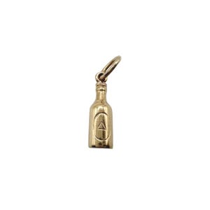 May include: A gold-colored bottle charm with a loop for a necklace or bracelet. The charm has a detailed bottle shape with a small triangle design on the front. The charm is made of a shiny, metallic material.