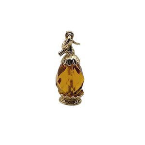 May include: A gold charm shaped like a miniature perfume bottle featuring a faceted amber-colored glass body. The piece includes a decorative gold metal cap and base with scalloped edges and a small jump ring at the top for attachment.
