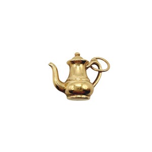 May include: A polished gold charm shaped like a miniature teapot. The charm features a curved spout, a rounded body, a lid with a small knob, and a handle with an attached circular jump ring for hanging. The surface is smooth and reflective.