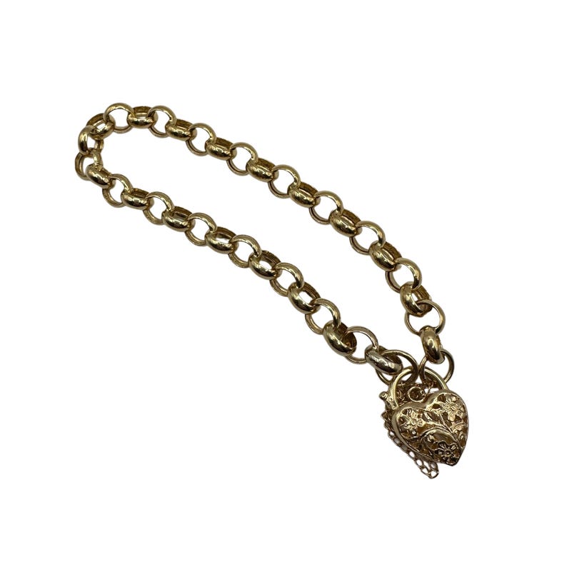 Op de afbeelding: Een goudkleurige ketting met een hartvormige hanger. De ketting heeft een ketting van ronde schakels en een decoratief hartvormig slot met bloemmotieven. De hanger is ongeveer 2,5 cm lang.