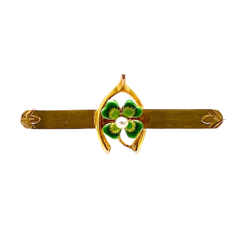 May include: A gold-toned pin with a green four-leaf clover design and a pearl in the center. The clover is set in a horseshoe-shaped frame.
