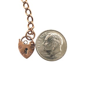 May include: A heart-shaped, antique copper-colored padlock with a keyhole and decorative rivets, attached to a matching chain. A U.S. dime is next to the padlock for size comparison. The dime is dated 2021.