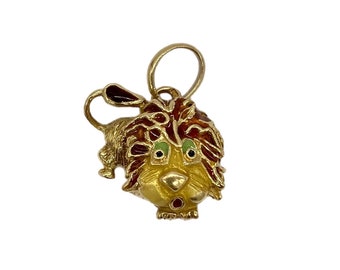 May include: A gold-toned charm with a lion design. The lion has red and brown fur, green eyes, and a yellow face. The charm is detailed with enamel paint.