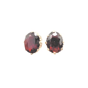 May include: A pair of gold earrings with red gemstone accents. The earrings feature a round, faceted gemstone set in a gold setting with a decorative border.