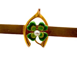 May include: A gold horseshoe charm with a green four-leaf clover enamel design and a white pearl in the center.