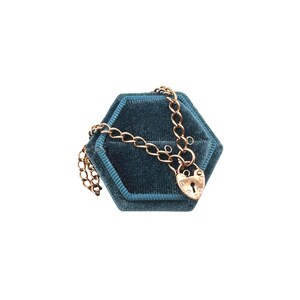 May include: A gold-colored necklace with a heart-shaped padlock pendant rests on a teal velvet jewelry box. The necklace chain is made of small, interconnected links. The padlock has a keyhole and decorative details.
