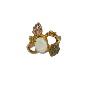May include: A gold ring with an oval opal gemstone and three green and gold leaf accents.