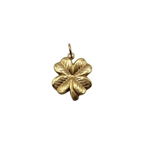 May include: A gold-toned four-leaf clover pendant featuring etched line details on each leaf and a small circular jump ring at the top for attachment. The surface of the metal charm has a polished finish with visible engraved textures.