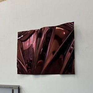 Könnte beinhalten: Eine große, abstrakte Wandskulptur aus einem metallischen Material in einem tiefen, satten Burgunderrot. Die Oberfläche der Skulptur ist hochreflektierend und wirkt gefaltet oder zerknittert, was einen dynamischen und strukturierten Effekt erzeugt.