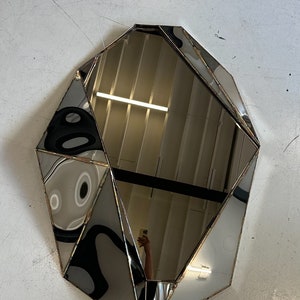 May include: A geometric-shaped mirror with a silver frame. The mirror is made of multiple pieces of glass that are joined together to create a unique design.