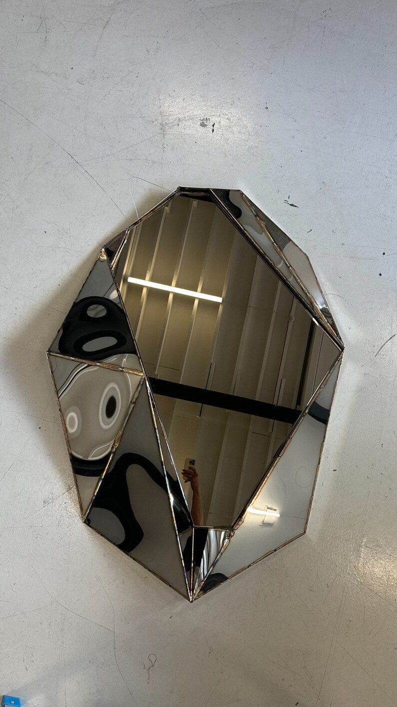 May include: A geometric-shaped mirror with a silver frame. The mirror is made of multiple pieces of glass that are joined together to create a unique design.