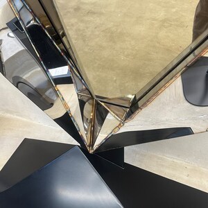 May include: A large, silver, geometric mirror with a black base. The mirror is made of multiple pieces of metal that are joined together to create a unique and modern design.