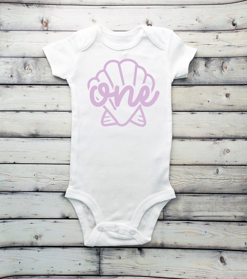 May include: White baby onesie with a purple seashell design and the word "one" inside the shell.