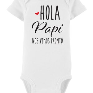 May include: White baby onesie with black text that reads "Hola Papi Nos Vemos Pronto" with a small red heart before the word "Hola".