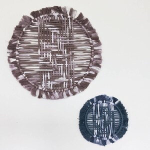May include: Two circular wall hangings made of woven yarn with fringe. The larger one is brown and white, and the smaller one is dark blue and white.