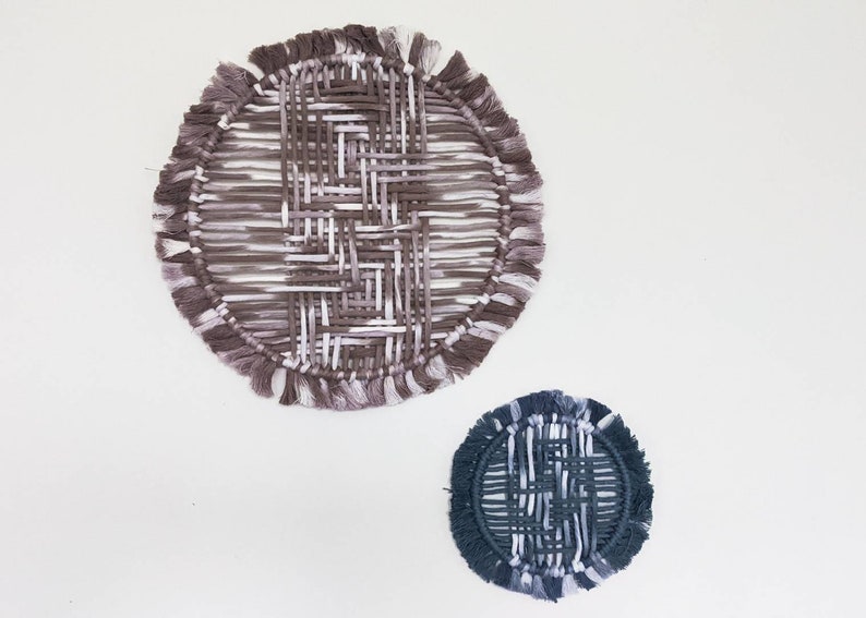 May include: Two circular wall hangings made of woven yarn with fringe. The larger one is brown and white, and the smaller one is dark blue and white.