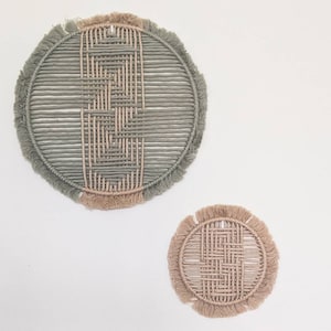 May include: Two circular wall hangings made of woven rope with fringe. The larger one is green and the smaller one is beige.