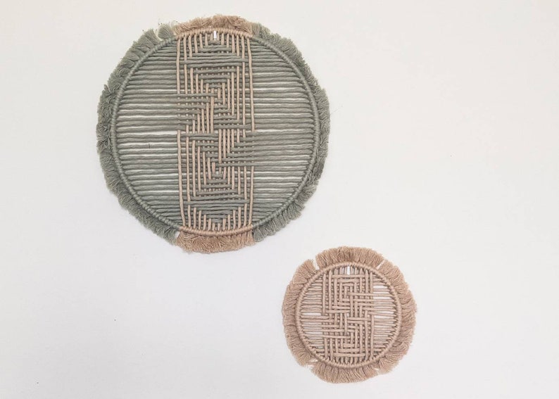 May include: Two circular wall hangings made of woven rope with fringe. The larger one is green and the smaller one is beige.