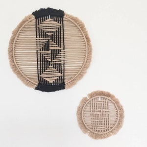 May include: Two circular wall hangings made of natural fibre rope with a black geometric pattern woven into the centre. The larger hanging is approximately 12 inches in diameter and the smaller hanging is approximately 6 inches in diameter.