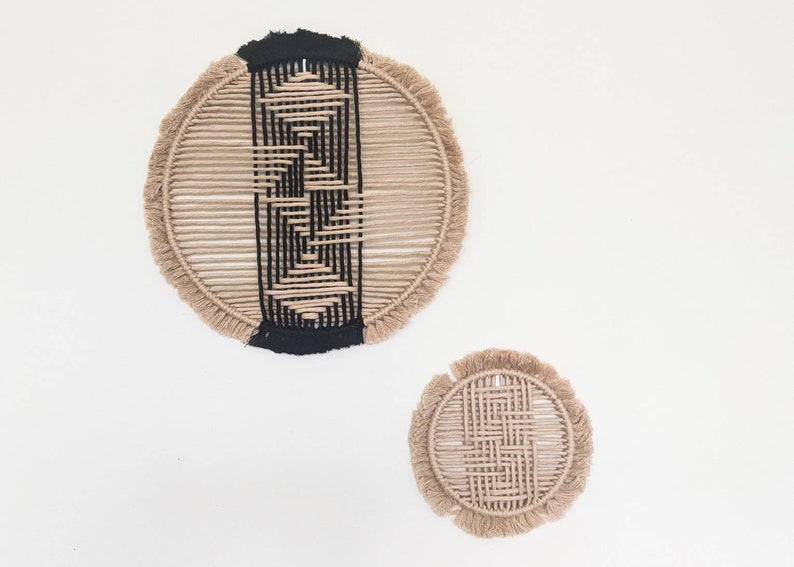 May include: Two circular wall hangings made of natural fibre rope with a black geometric pattern woven into the centre. The larger hanging is approximately 12 inches in diameter and the smaller hanging is approximately 6 inches in diameter.