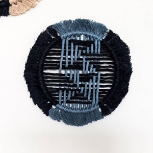 May include: A round, woven wall hanging with a black and blue geometric pattern. The hanging has a fringe border.