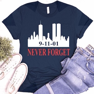 May include: A navy blue t-shirt with a white silhouette of the New York City skyline and the text "9-11-01 NEVER FORGET" in red.