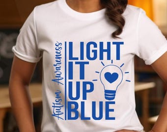 May include: White t-shirt with blue text that reads "Light It Up Blue" and "Autism Awareness". A blue lightbulb with a heart inside is included in the design.