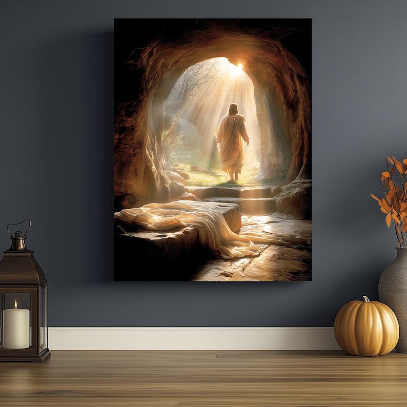 May include: A canvas print with a religious theme shows a figure in a white robe exiting a cave, illuminated by sunlight. The scene features a stone tomb with draped fabric, steps, and a bright light at the cave's entrance. The artwork conveys a sense of hope and resurrection.