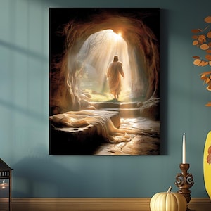 May include: A canvas print showing a figure in a white robe exiting a cave, illuminated by sunlight. The artwork uses a warm colour palette with detailed textures, creating a peaceful and spiritual scene. The image is mounted on a wall.