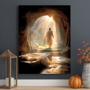 May include: A religious art print shows a figure in a white robe emerging from a cave into bright sunlight. The artwork features a stone tomb with draped fabric, steps, and a natural outdoor setting. The overall colour palette is warm, with golden and brown tones.