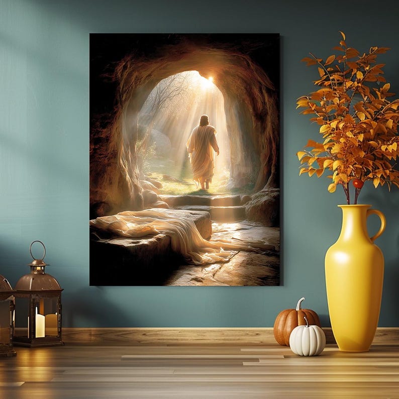 May include: A canvas print shows a figure emerging from a cave into sunlight. The image features a person in a white robe, with light rays shining through the cave entrance. A yellow vase with autumn foliage and pumpkins are in the foreground.