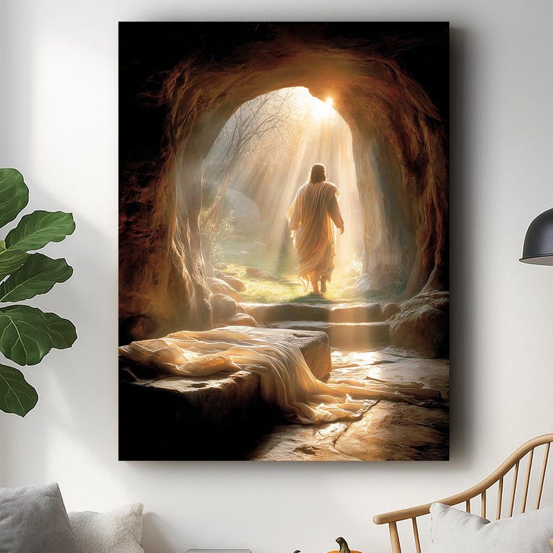 May include: A canvas print showing a religious scene. A figure in a white robe walks out of a cave towards bright sunlight. The cave interior is brown, and a stone slab with draped fabric is in the foreground.