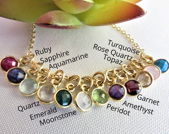 May include: A gold chain necklace with 12 gemstone charms, each charm is labeled with the name of a gemstone. The gemstones are: Ruby, Sapphire, Aquamarine, Quartz, Emerald, Moonstone, Peridot, Amethyst, Garnet, Turquoise, Rose Quartz, and Topaz.