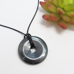 May include: A black leather cord necklace with a round, black hematite pendant. The pendant has a hole in the center.