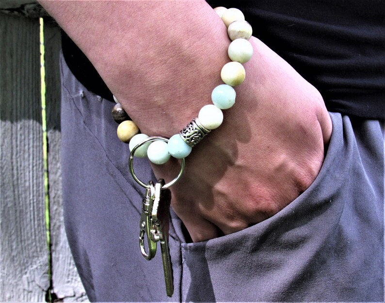 May include: A beaded bracelet with a silver charm and a key chain attached. The bracelet is made of light blue, white, and brown beads.