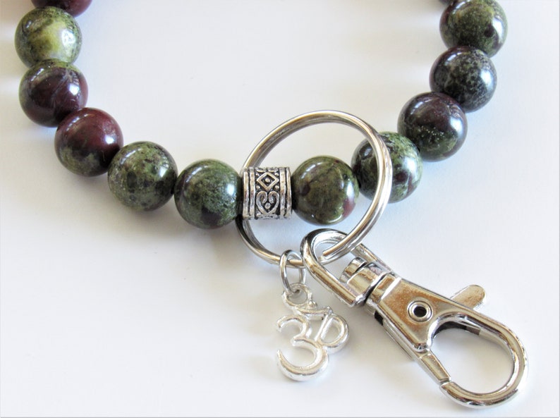 May include: A green and brown beaded keychain with a silver key ring, a silver charm with an Om symbol, and a silver clasp.