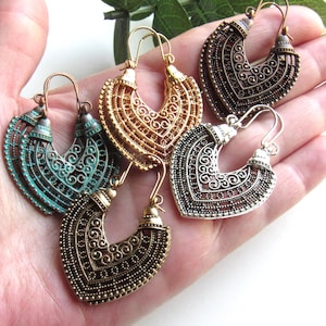 May include: A collection of ornate, open-work earrings in various metallic finishes, including gold, silver, bronze, and teal. The earrings feature a crescent shape with intricate filigree designs and are displayed on a hand.
