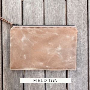 May include: A rectangular zippered pouch in a field tan color with a weathered, textured finish. The pouch features a black zipper closure along the top edge and a thin brown leather pull tab attached to the metal zipper slider for easy opening.