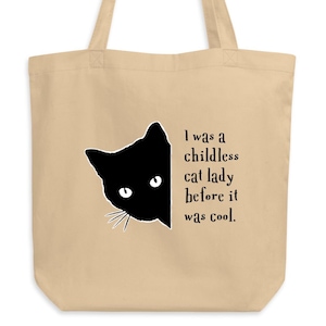 May include: A beige tote bag with a black cat silhouette peeking out from the side. The text on the bag reads "I was a childless cat lady before it was cool."