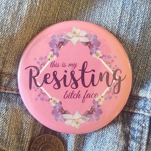 May include: Pink button with a floral design and the text "This is my Resisting bitch face".