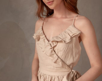 May include: A woman wearing a beige linen dress with a ruffled neckline and a tie at the waist. The dress has a relaxed, flowy fit.