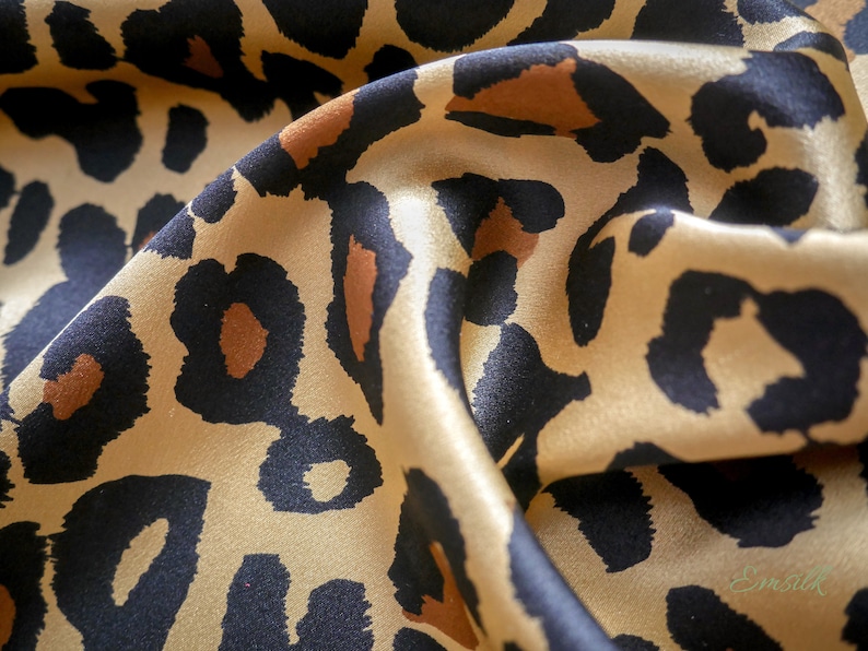 May include: Close-up of a gold and black leopard print fabric. The fabric is soft and silky, with a subtle sheen.