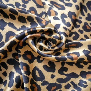 May include: A close-up of a gold and black leopard print fabric. The fabric is made of satin and has a soft, luxurious feel.