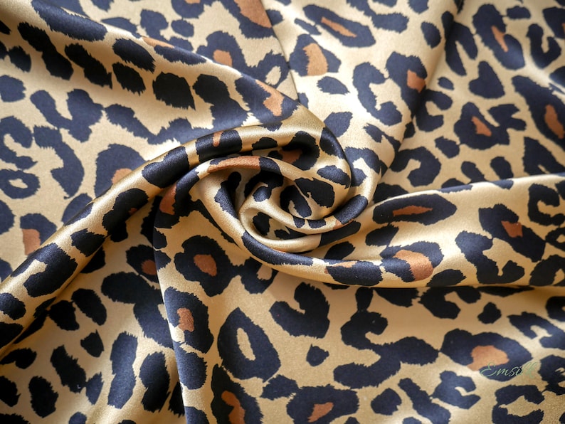 May include: A close-up of a gold and black leopard print fabric. The fabric is made of satin and has a soft, luxurious feel.