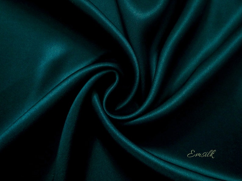 Puede incluir: Primer plano de una tela verde azulado oscuro, mostrando su textura suave y sedosa. La tela est&aacute; drapeada y doblada, creando curvas y pliegues suaves.