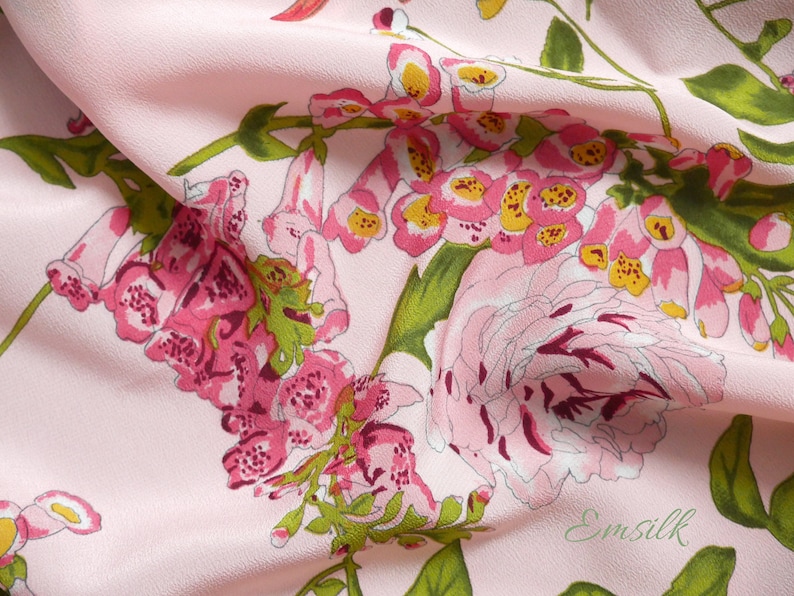 May include: Pink fabric with a floral print featuring pink, white, and yellow flowers. The fabric has a subtle texture and is draped over a surface.