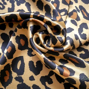 May include: A close-up of a gold and black leopard print fabric. The fabric is made of silk and has a soft, luxurious feel.