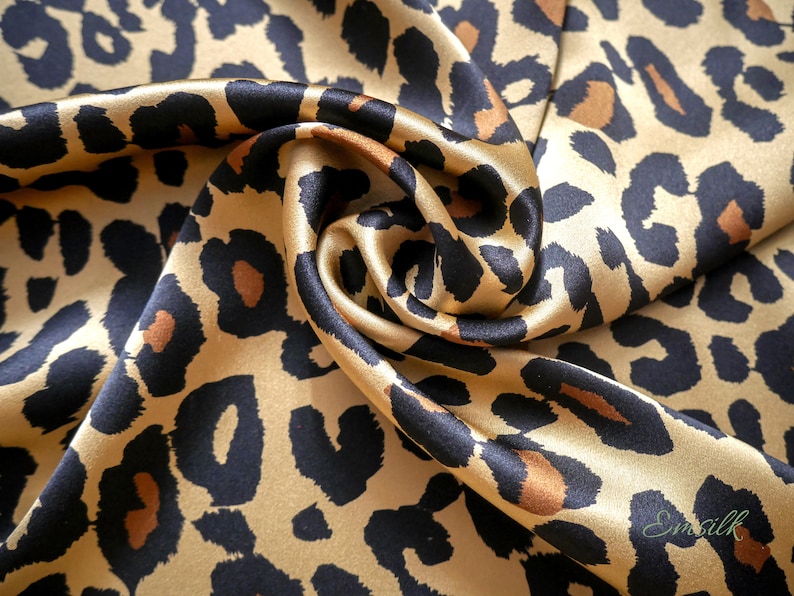 May include: A close-up of a gold and black leopard print fabric. The fabric is made of silk and has a soft, luxurious feel.