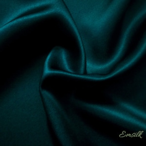 Puede incluir: Una tela de seda verde azulado oscuro con una textura suave y lujosa. La tela est&aacute; drapeada y doblada, creando l&iacute;neas suaves y fluidas.