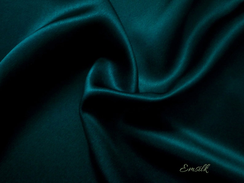 Puede incluir: Una tela de seda verde azulado oscuro con una textura suave y lujosa. La tela est&aacute; drapeada y doblada, creando l&iacute;neas suaves y fluidas.